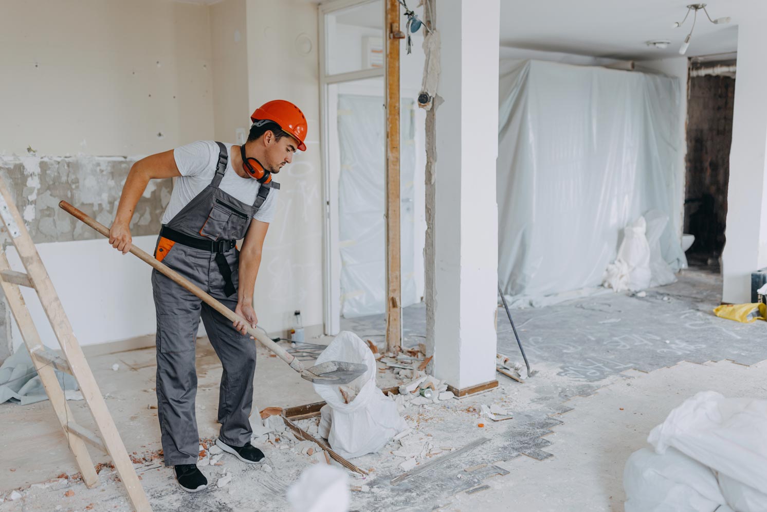 Male construction worker is using a shovel to fill up a big bag with construction residue.