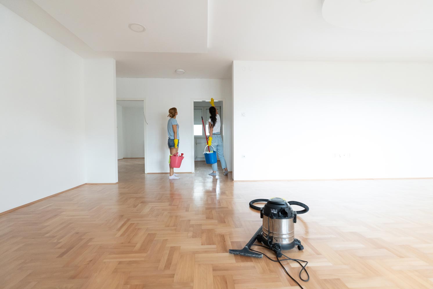 Two individuals are cleaning an empty, white-walled room